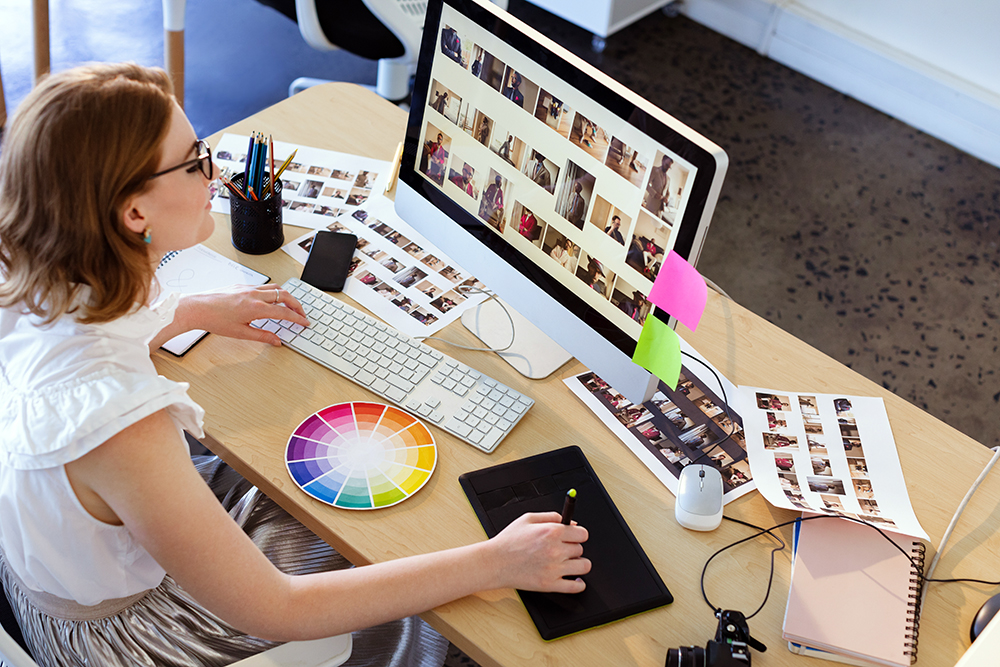 High Angle View Of Young Caucasian Female Graphic Designer Working On Graphic Tablet And Computer At Desk In Office. High angle view of young Caucasian female graphic designer working on graphic tablet and computer at desk in office.